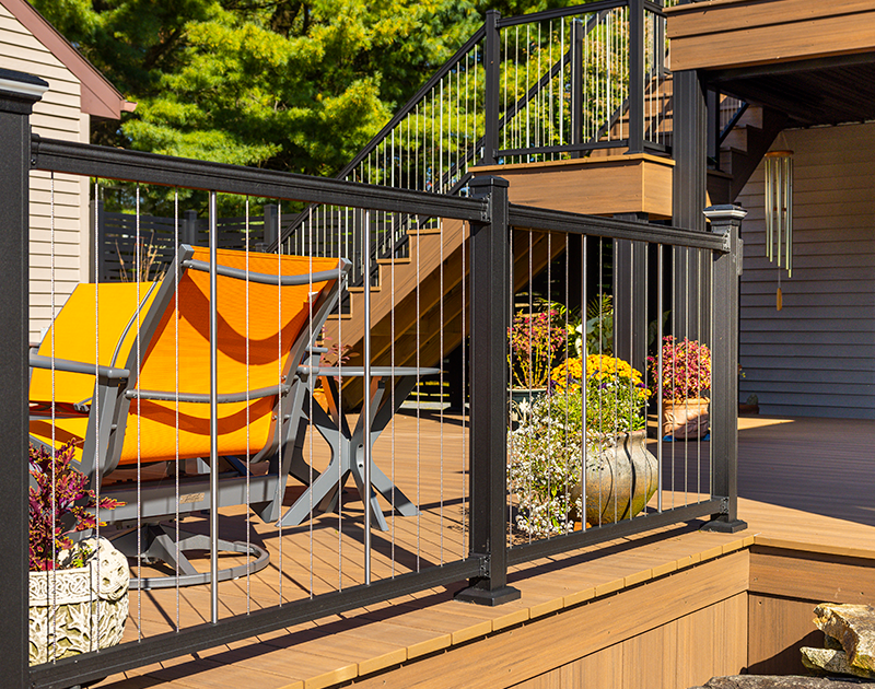 Composite deck with lush greenery, orange patio furniture and a vertical cable deck railing